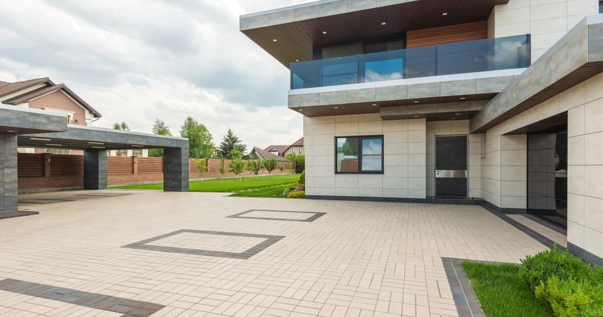 Modern double-storey house with a tiled driveway and lawn under a bright sky