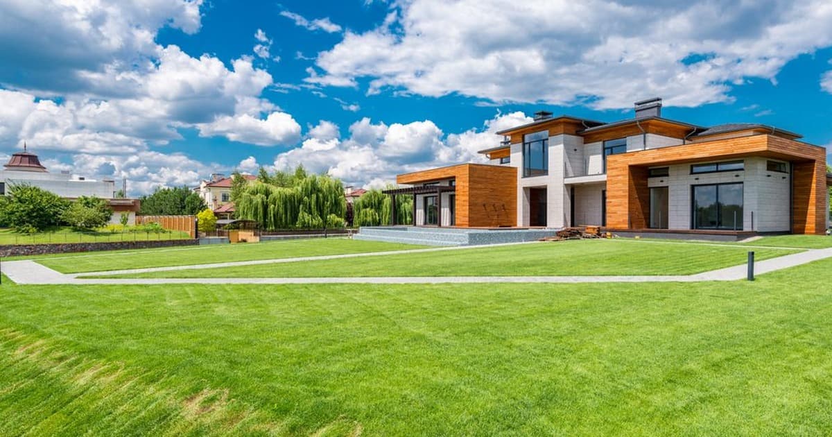 Modern two-storey villa with a large green lawn under a bright blue sky