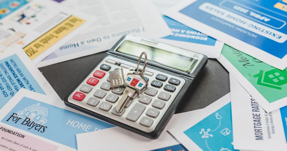 Calculator with house keys on property buyer flyers, symbolizing the cost calculations behind a plot purchase